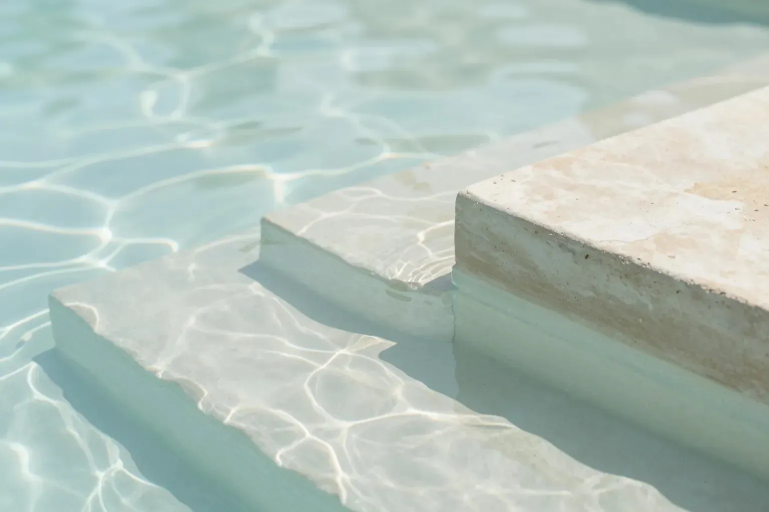 Calm water casting light patterns across pale stone pool steps.